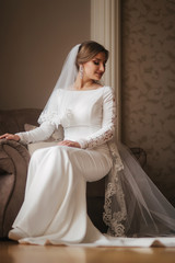 Gorgeous bride sitting on the chair at the home. Beautiful woman in wedding dress