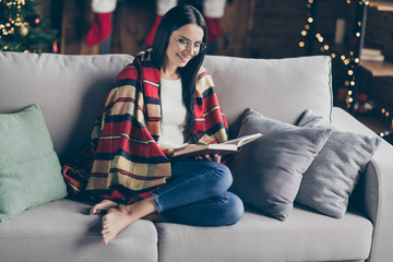 Full size photo of positive girl have christmas celebration time sit divan barefoot in house with x-mas festive decorative lights ornaments read fiction magic book indoors enjoy newyear spirit