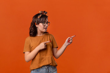 Smiling brunette woman in a t-shirt, beautiful headband and eyeglasses pointing with her fingers at...