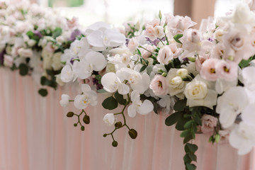 A long composition of fresh luxury flowers on the wedding table of the groom and bride