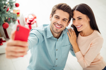 Close up photo of two people cheerful spouses making selfie on cell phone sitting on floor enjoy christmas time x-mas holidays in house indoors
