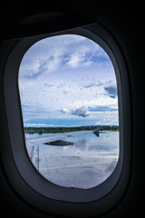 Airplane window covered with rain drops. And the view of the airplane right wing and outdoor at the airport runway. Selective focus.  Copy space.