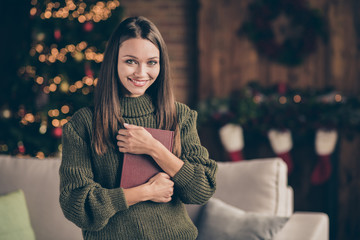 Close up photo of positive cheerful brown hair girl in knitted jumper hold fiction book enjoy her jolly christmas celebration feel content in house full of newyear x-mas decorations lights indoors