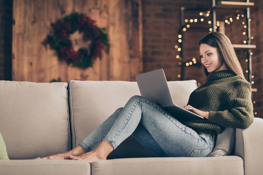 Full length profile side photo of charming positive girl enjoy her christmas time vacations lying on divan type email to her friends send congratulations with newyear use laptop in house indoors