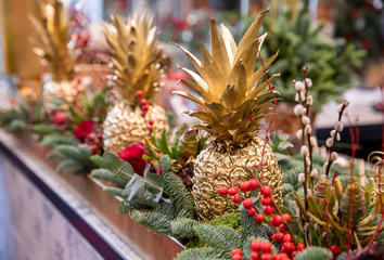 Winter decor. Beautiful arrangement of golden colored pineapples, red roses, natural sprigs of blue...