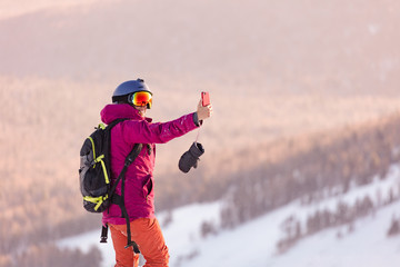 Young Beautiful female skier taking a selfie. Sporty woman taking selfie without snowboard at winter resort. Skiers in winter nature.  sunrise light, edit space. 