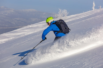 freerider in a bright suit rides fast skiing with large splashes of snow on a sunny day. very high...