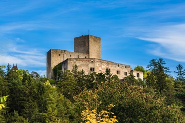 Fototapeta na wymiar Landstejn, Czech Republic - September 29 2019: View of a medieval knights castle made of stone standing on a green hill surrounded with trees. Bright sunny day with blue sky and white clouds.