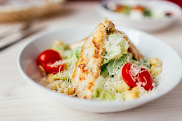 Fresh healthy caesar salad with chicken on white wooden table with fork and knife. Top view. Selective focus.