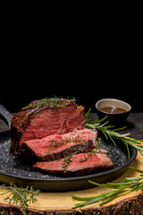 Sous-vide grilled beef steak with herbs in cast-iron skillet on wooden plate.