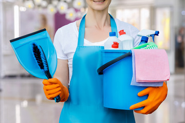 The cleaning lady standing with a bucket and with tool .