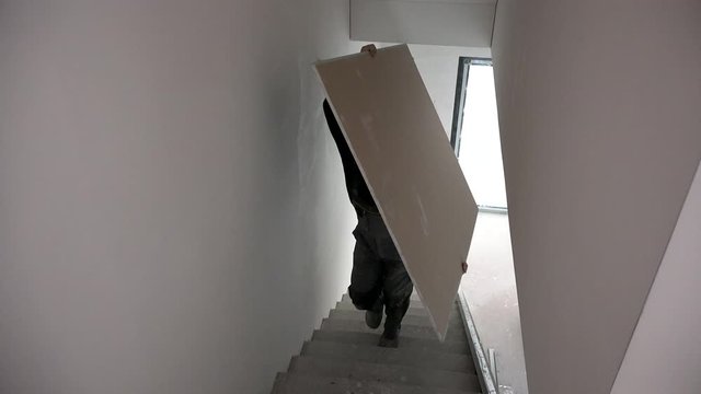Unrecognizable man carry sheet of gypsum plasterboard on stair