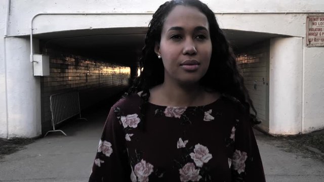 Slow motion clip of a happy upbeat mixed race African American woman walking directly towards the camera to a close up transition from a dark underpass in an urban environment.