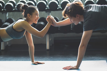 Asian men and women wear a push-up exercise suit and hold hands in the fitness room with a black dumbbell background.