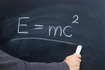 hand of a young person writing the Einstein formula on a blackboard