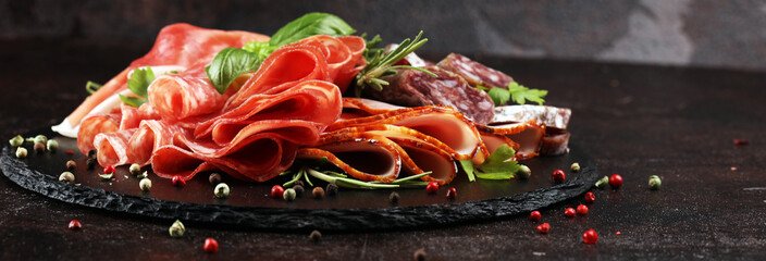Marble cutting board with prosciutto, bacon, salami and sausages on wooden background. Rustic Meat...
