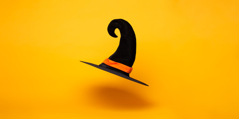 Black witch hat on blank orange background, space for text.