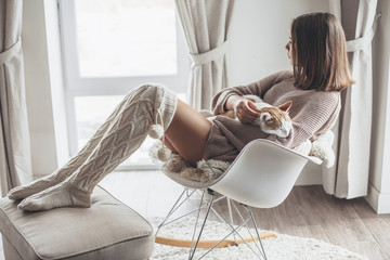 Girl in winter sweater sitting with cat on armchair