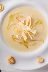Conceptual cream soup in a white plate on a white table in a restaurant, cool plan. space