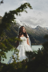 Beautiful Kazakh Asian bride in a white dress and veil against the backdrop of a lake in the mountains landscape, wedding photo