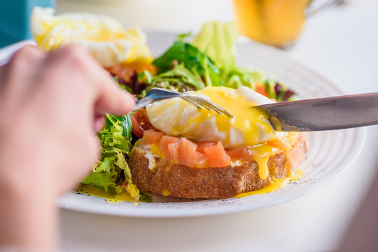 Girl eats toasts with salmon and poached egg, served with fresh salad in restaurant. Healthy breakfast. Close-up. Space. Series of photos