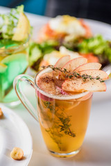 Autumn tea with rosemary, cinnamon, decorated with apple slices in transparent cup on white table in restaurant. Close-up. Space