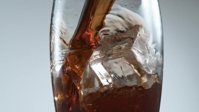Pouring cola over ice in super slow motion