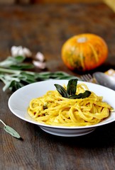 pasta spaghetti with pumpkin-cream sauce with sage and chips of sage leaves. autumn dish. sunny day, the rays of the sun.