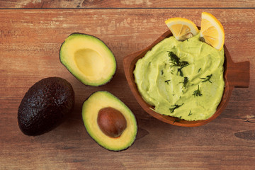 Fresh avocado cream in brown bowl and fresh sliced avocados on brown wooden background. Top view. Copy space. Vegetarian food concept, vintage style, avocado background.
