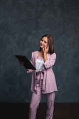 A business girl in a light suit holds a black folder in her hands and talks on the phone. Portrait of a beautiful girl on a dark gray background, space for text. office worker
