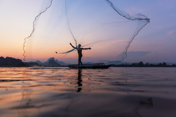 Asian fishermen throwing fishing net during twilight on wooden boat at the lake. Concept...