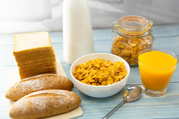 Breakfast served with orange juice, croissants, bread, cereals and milk  on wooden table in the kitchen at home. Healthy food.