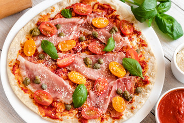 Italian pizza with prosciutto ham, capers, cherry tomatoes, parmesan cheese and decorated with basil leaves.