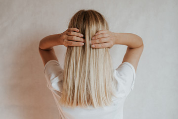 Fototapeta premium Blond hair woman posing near a light wall. Beautiful young caucasian girl. Hand gestures. Emotion. Casual clothing. Studio model in work. Strong woman, future is female. Jeans and white blank t-shirt