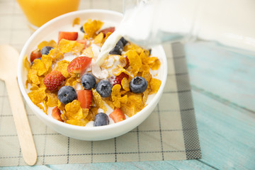 Healthy breakfast. Pour milk from jug into cereal bowl and fruit on wooden table. Healthy food