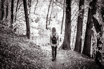 Woman in autumn forest, back view. Lonely adult girl walking away alone on path in fall park. Young...