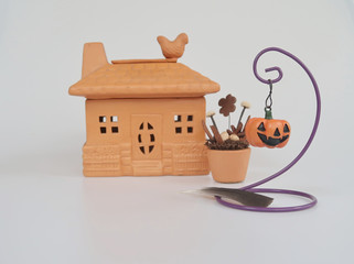 Halloween pumpkin hangs on wire binder hanger and a feather  near a clay house and flower plant  pot for decoration in Halloween concept 