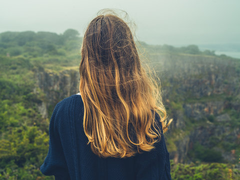 Young woman looking at rocky cliff on misty day