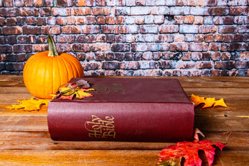reading large bible on fall day with orange pumpkin and autumn leaves