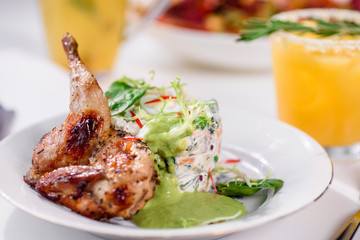 Tobacco chicken with salad on a white table in a restaurant. Tea and dessert on a blurred background. Large plna. Space