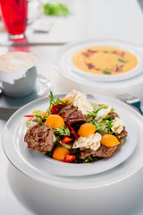 Business lunch - fresh vegetable salad with grilled meat and pumpkin cream soup in white plates on a white table in a restaurant. Close-up. Space