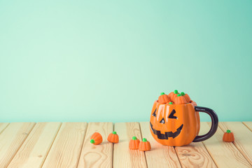 Halloween holiday concept with jack o lantern cup and pumpkin candy on wooden table