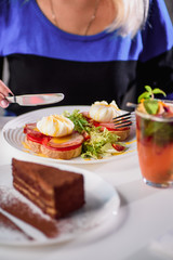 Woman eating toast with ham, tomato, poached egg and fresh salad in a restaurant. Healthy breakfast. Close-up. Space