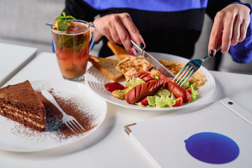 American breakfast - fried sausages, omelet and salad with vegetables on white plate, tea and chocolate dessert on white table in a restaurant. Close-up. Space. Lunch
