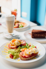 Toasts with ham, tomato and poached egg, served with fresh salad on white plate. Healthy breakfast on the table in the restaurant. Close-up. Space