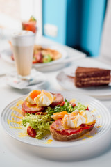 Toasts with ham, tomato and poached egg, served with fresh salad on white plate. Healthy breakfast on the table in the restaurant. Close-up. Space