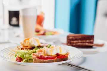 Toasts with ham, tomato and poached egg, served with fresh salad on white plate. Healthy breakfast on the table in the restaurant. Close-up. Space