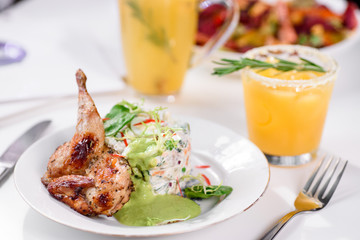 Tobacco chicken with salad on a white table in a restaurant. Tea and dessert on a blurred background. Large plna. Space