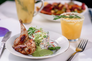 Tobacco chicken with salad on a white table in a restaurant. Tea and dessert on a blurred background. Large plna. Space