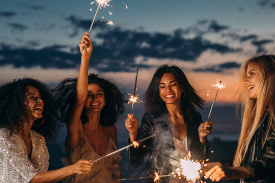Four happy women celebrating at sunset with sparklers